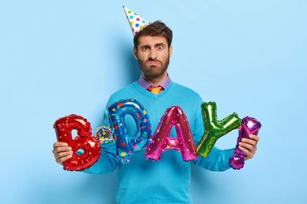 Dissatisfied birthday man holds colorful letter shaped balloons