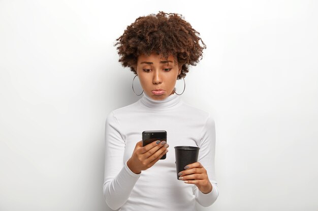 Dissatisfied black woman with curly hair, looks sadly at phone