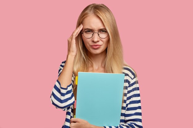 dissatisfied blonde college student posing against the pink wall