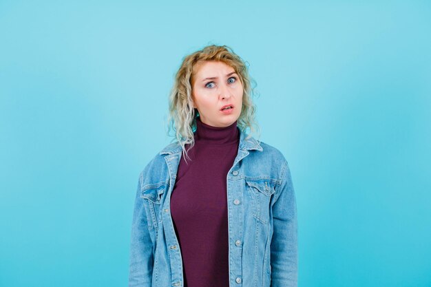 Dissatisfied blonde woman is looking at camera on blue background