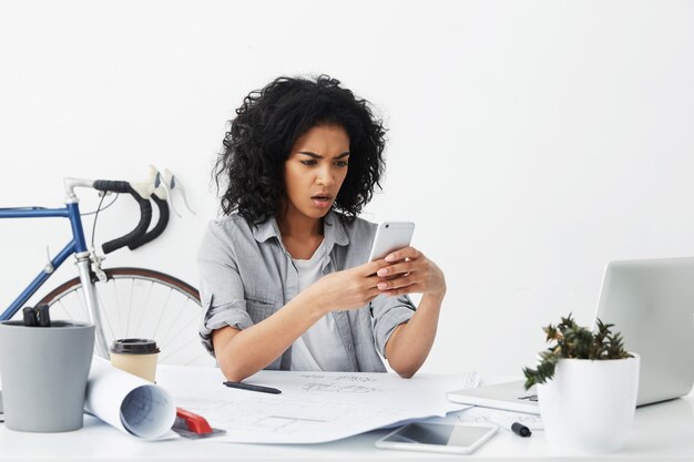 Dissatisfied business woman with dark skin and voluminous hair sitting at her office