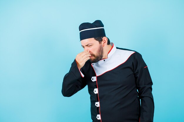 Dissatisfied chef is holding his nose on blue background
