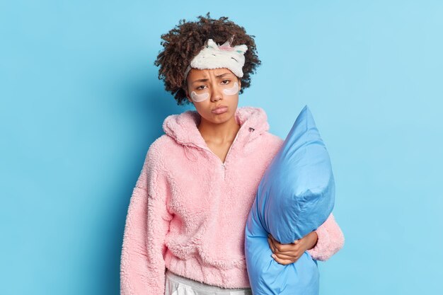 不満の縮れ毛の若いアフロアメリカ人女性は眠りたい枕を保持し、寝る準備をします