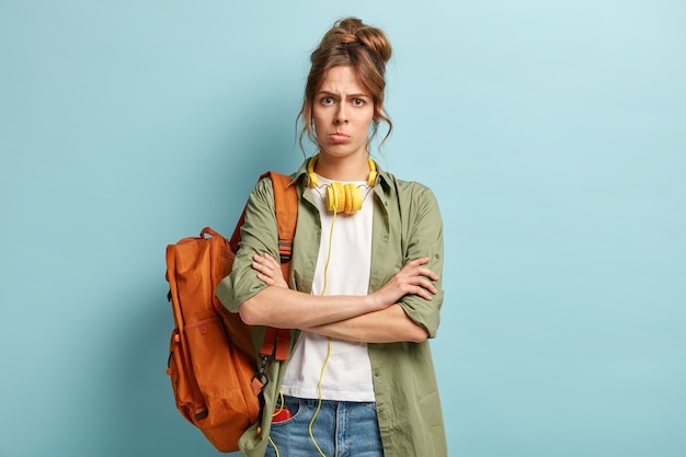 Dissatisfied female keeps arms folded, looks angrily at camera, doesnt want to have classes, carries rucksack