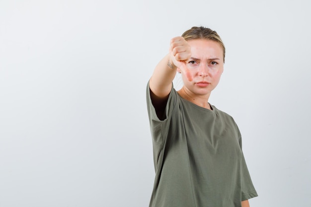 The dissatisfied girl is pointing down with her thumb on white background