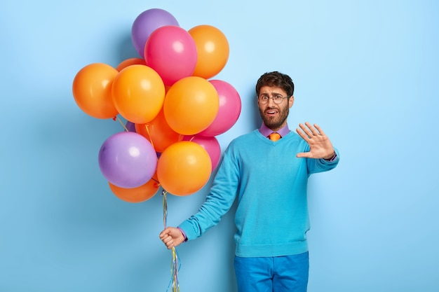 Dissatisfied guy with balloons posing in blue sweater