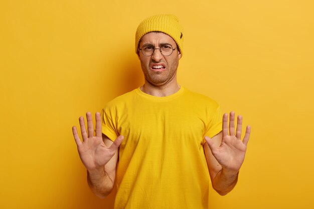 Dissatisfied man rejects, denies proposition, gets bad deal offer, says no with two palms pulled towards camera, refuses something, wears round spectacles