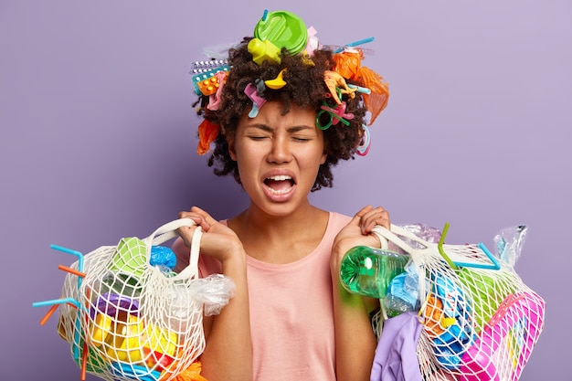 Free photo dissatisfied stressful afro american woman holds two bags full of garbage, cries from negative emotions, being tired after collecting litter, concerned and disturbed about ecological problem