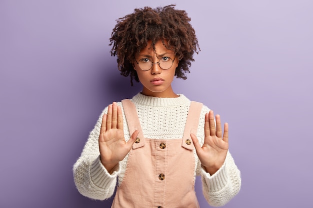 Free photo dissatisfied young woman with dark skin, curly hair, makes stop gesture, has angry facial expression