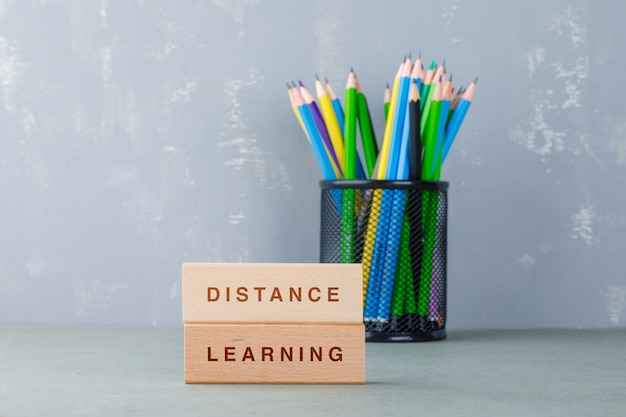 Distance education concept with wooden blocks with words on it, colorful pencils side view.