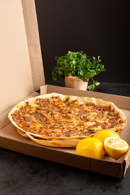 A distanced front view lahmacun dough with minced meat along with greens and lemon inside paper box tasty pastry meal