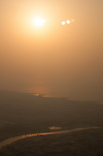 Distant shot of a river flowing near a town during daytime with a sun shining brightly in the sky