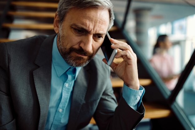 Distraught businessman communicating over mobile phone in the office