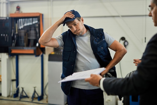 Free photo distraught car mechanic going through problematic paperwork with his manager in auto repair shop