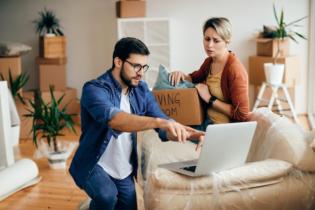 Distraught couple using laptop while moving into their new home