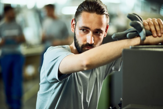 Distraught factory worker leaning on CNC machine while working in industrial building