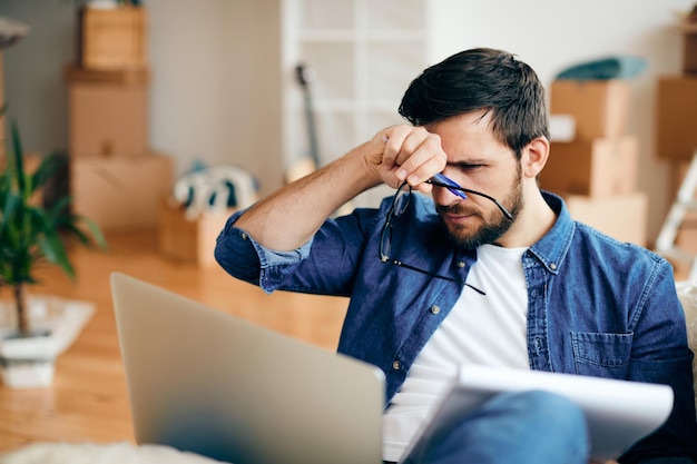 Distraught man reading an email on laptop while moving into a new home