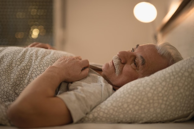 Distraught senior man thinking of something while lying down in bed at night