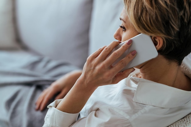 Distraught woman resting on the sofa and communicating over mobile phone