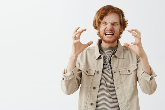 Distressed and angry bearded redhead guy posing against the white wall