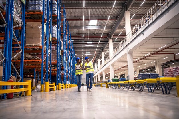 Distribution warehouse interior with workers wearing hardhats and reflective jackets walking in storage area