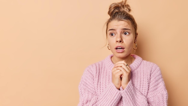 Free photo disturbed worried young woman keeps hands in prayer gesture hopes everything will be okay feels anxious about something wears warm knittedd sweater isolated over beige background copy space area