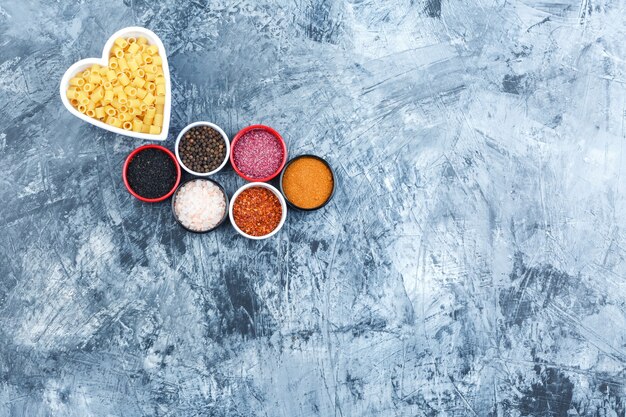 Ditalini pasta in a white bowl with spices top view on a grey plaster background