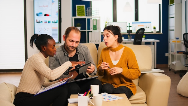 Diverse businesspeople analysing financial project during corporate meeting. Multiethnic employees group listening colleague sharing ideas discussing new marketing plan comparing data from tablet.