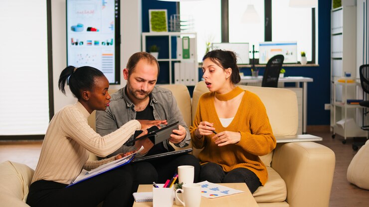 Diverse businesspeople analysing financial project during corporate meeting. Multiethnic employees group listening colleague sharing ideas discussing new marketing plan comparing data from tablet.