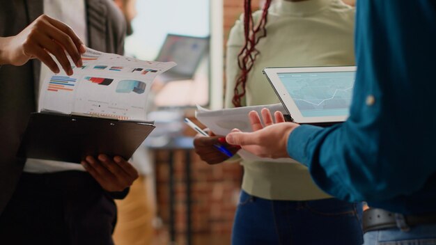 Diverse colleagues working on business partnership with charts information and data research, planning group presentation. Analyzing graphs report with coworkers on files and tablet. Close up.