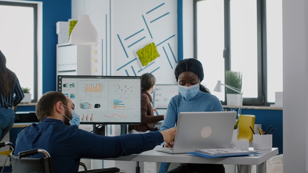 Diverse coworkers with protection face masks working together in new normal workplace during pandemic