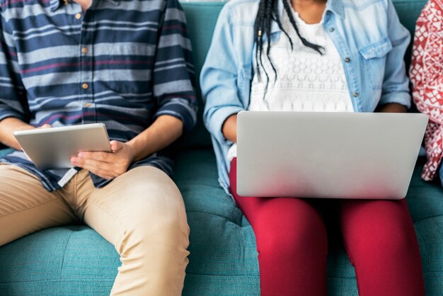 Diverse friends sitting on couch using laptop and tablet