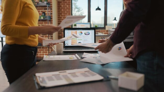 Diverse group of people doing teamwork to plan sales analysis, researching documents with charts and statistics in company office. Workmates brainstorming ideas to develop expertise.