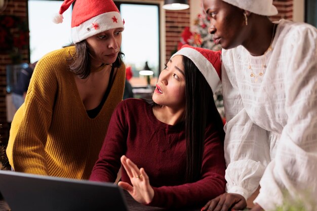 クリスマス ツリーと装飾のお祝いオフィスで事業計画に取り組んでいる女性の多様なグループ。チームワークを行い、季節の休日の飾りでクリスマスの時間を祝います。