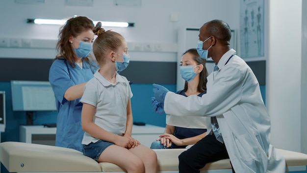 Diverse medical team analyzing radiography results with mother and child in cabinet. General practitioner and nurse explaining x ray scan diagnosis to woman and small girl at appointment.