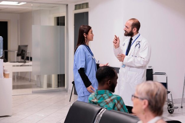 Free photo diverse medical team talking about healthcare support in hospital reception, discussing about patients and appointments at medical facility lobby. doctor and nurse in waiting room area.