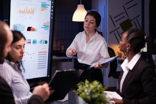 Diverse multiethnic business teamwork overworking in office meeting room analyzing financial graphs late at night