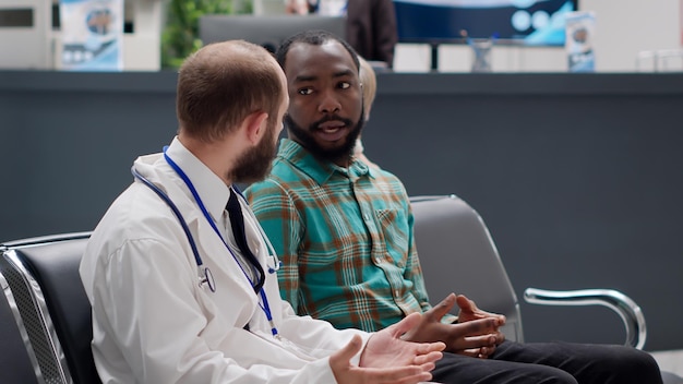 Free photo diverse people doing consultation exam in hospital reception area, talking about disease and treatment in waiting room lobby. physician and patient chatting about diagnosis at facility.