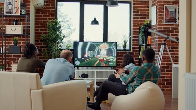 Diverse people having fun with video games online on tv console, playing gaming competition or challenge. Using gameplay to enjoy gathering with friends at home, drinking beer.