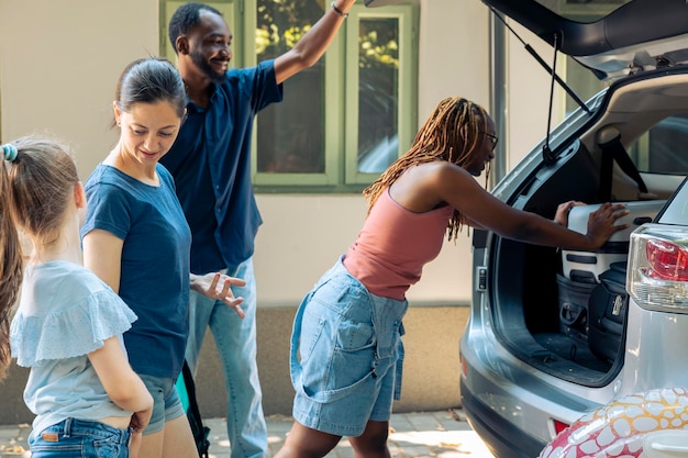 自動車のトランクに荷物を積み込み、夏休みに旅行する多様な人々。子供と多様な友人を持つ母親は、スーツケースのバッグを車に乗せ、休暇の遠征に出かけます。