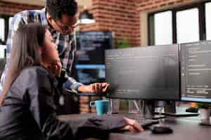 Free photo diverse programmers discussing about html code compiling discovers errors, standing in front of multiple screens in startup office. software developers working on server interface development.