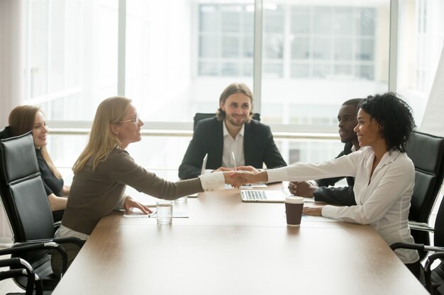 Diverse smiling businesswomen shaking hands greeting at multiracial group meeting