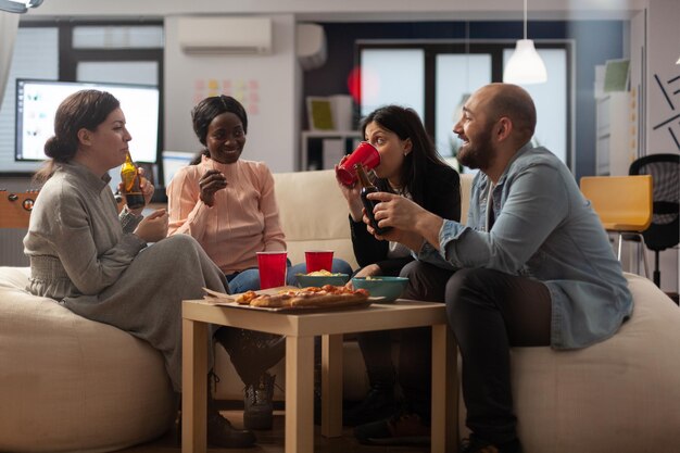 다양한 동료 팀이 퇴근 후 사무실에서 술을 마시며 맥주와 피자 스낵을 즐기며 즐거운 시간을 보내고 있습니다. 퇴근 후 여가 활동과 술과 함께 토론을 즐기는 직장 동료.