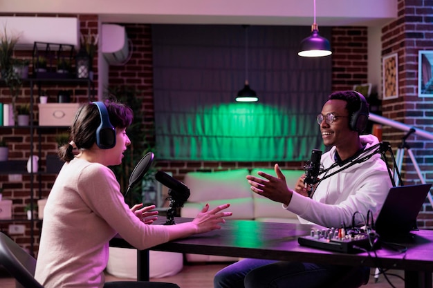 Diverse team of people working in studio to record podcast show, using camera and sound equipment. Man and woman having fun with chat on live broadcast for social media channel.