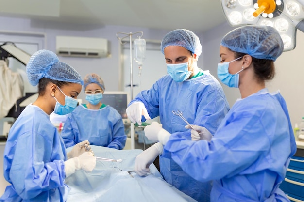 Team eterogeneo di assistenti chirurghi e infermieri professionisti che eseguono interventi chirurgici invasivi su un paziente in ospedale chirurghi di sala operatoria parlano e usano strumenti real modern hospital