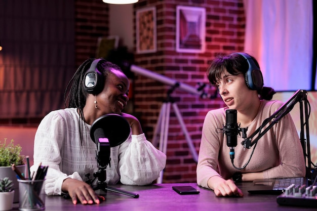 Diverse team of women enjoying podcast conversation in studio, filming online vlog and chatting for social media content. Female bloggers recording show episode at livestream station.