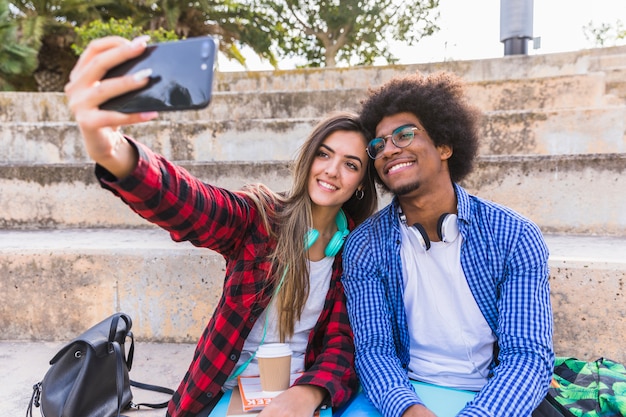 スマートフォンでselfieを取って階段の上に座って多様な若い学生カップル