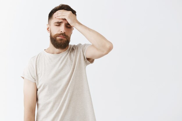 Dizzy bearded man posing against the white wall