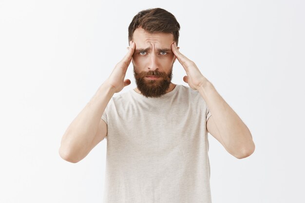 Dizzy bearded man posing against the white wall