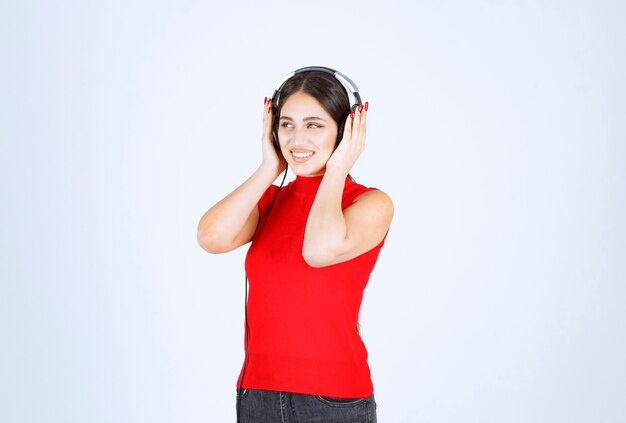 ヘッドフォンを着て、良い音楽を聴いている赤いシャツを着た DJ の女の子。